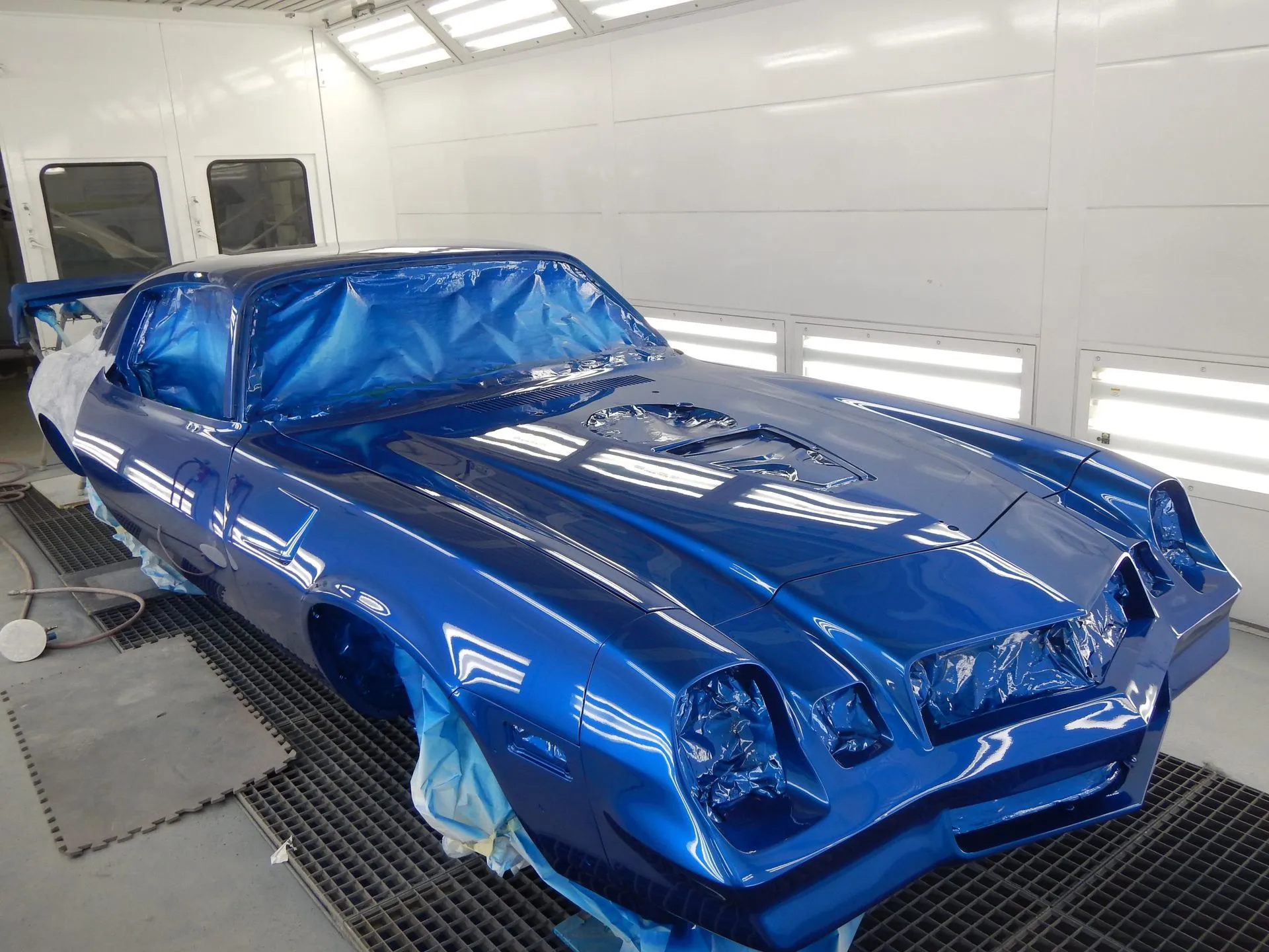 Blue classic sports car masked for painting in a white auto body shop