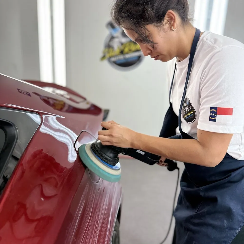Detailing technician polishing a red car with a buffer in a bright workshop