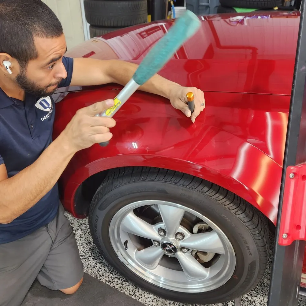 Mechanic using a hammer and tool on a red car’s front fender near the wheel