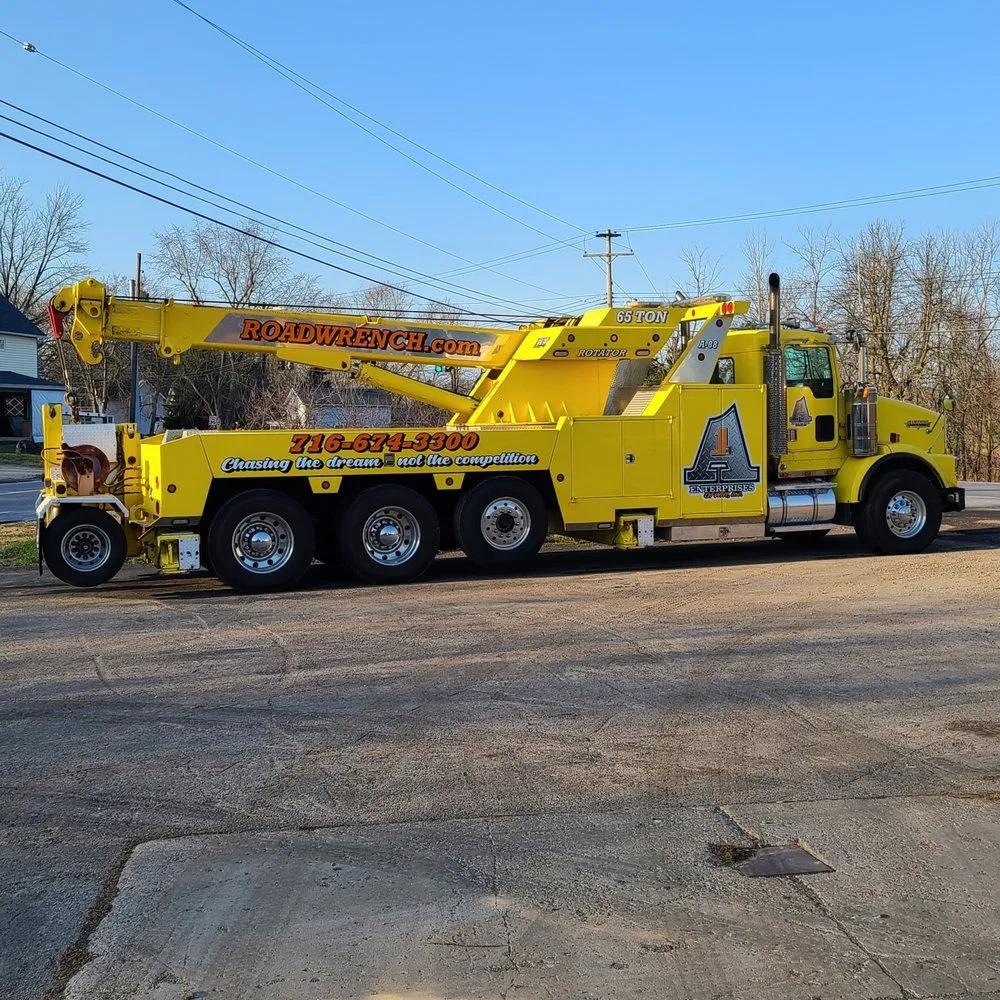Yellow tow truck with extended boom parked on a street under a clear blue sky.