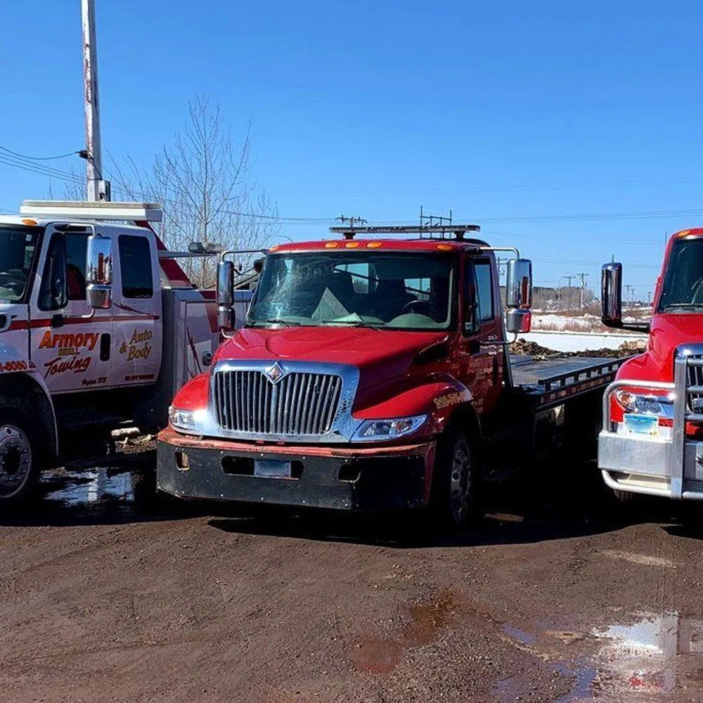 Red tow trucks parked in a muddy lot under a clear blue sky