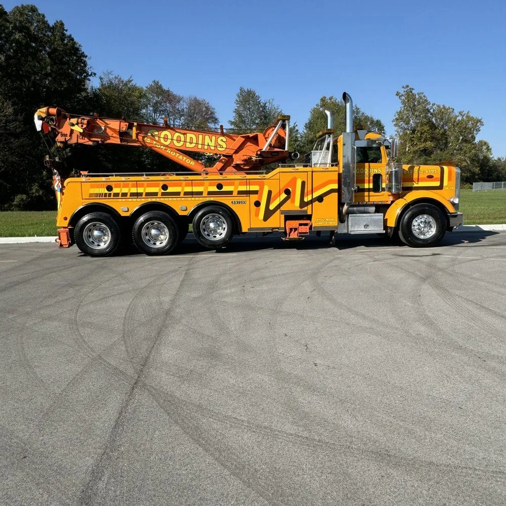 Yellow heavy-duty tow truck with an extended crane parked on pavement under a clear blue sky.