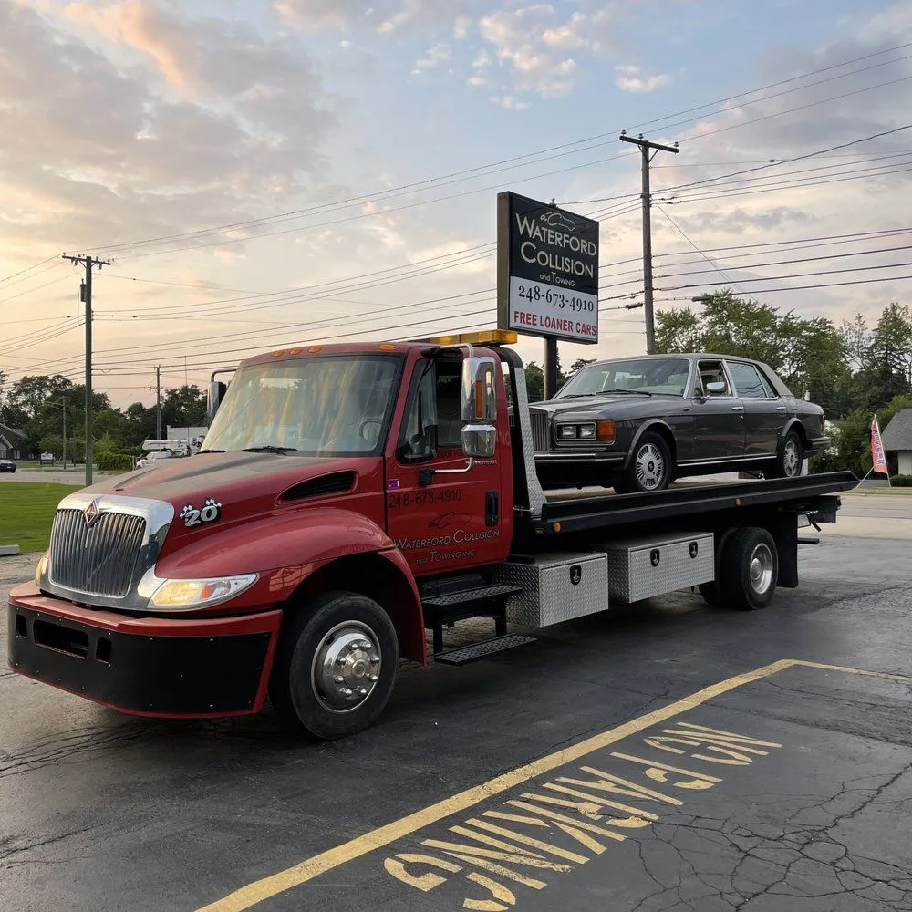 Red flatbed tow truck carrying a silver SUV on a street at dusk