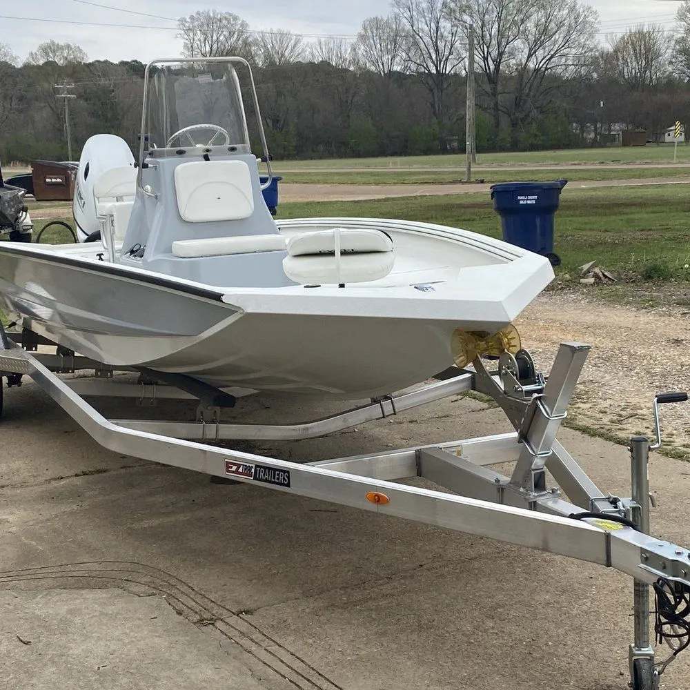 White center-console boat on a trailer parked on a concrete driveway with grass and trees in the background