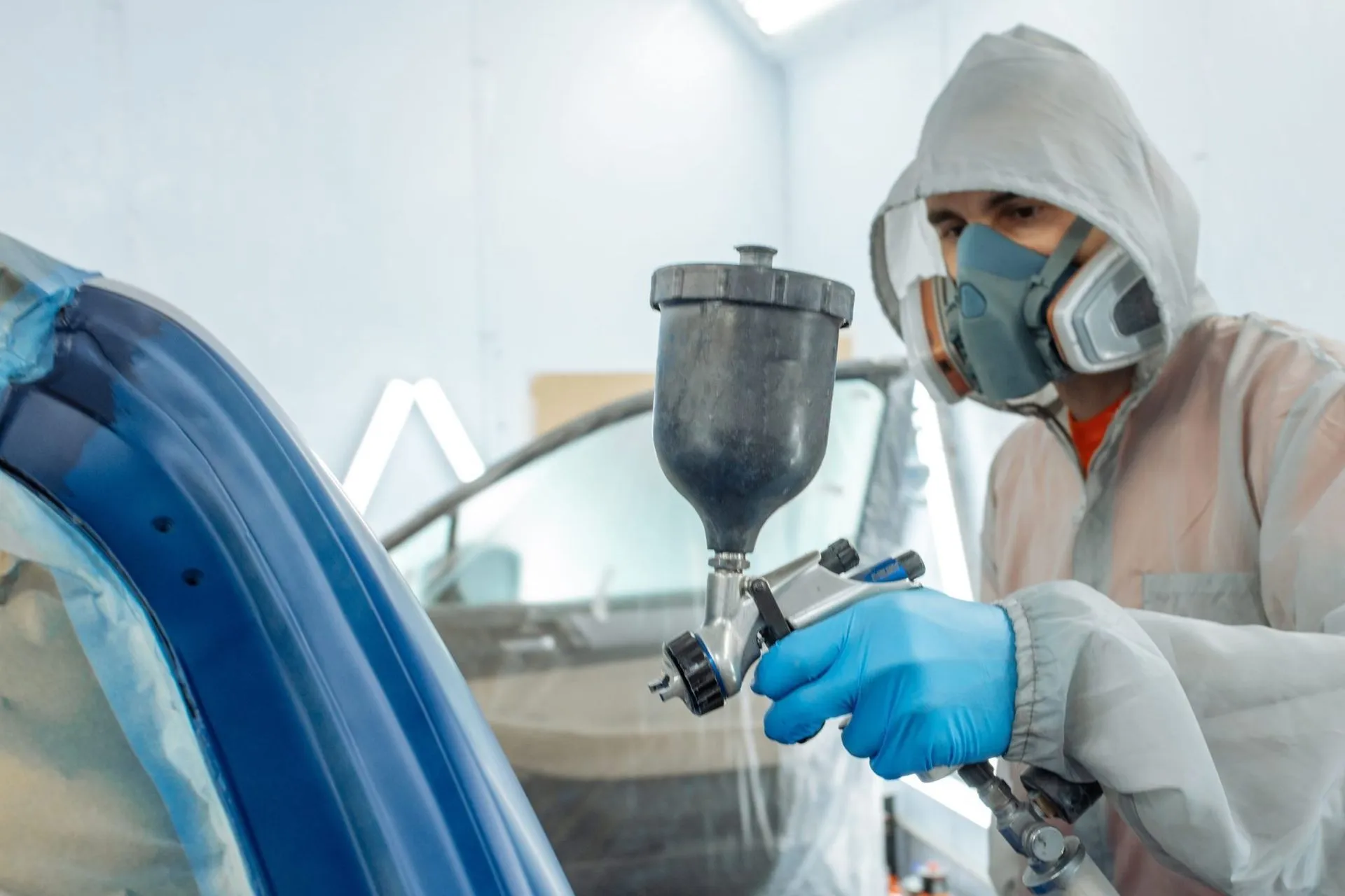 Painter in protective gear spray-painting a blue car in a workshop