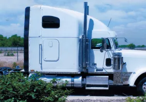 White semi-truck cab parked outdoors on a grassy roadside under a blue sky