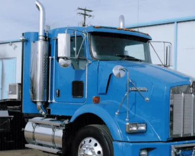 Blue semi-truck parked outdoors near a fence, shown in side view.