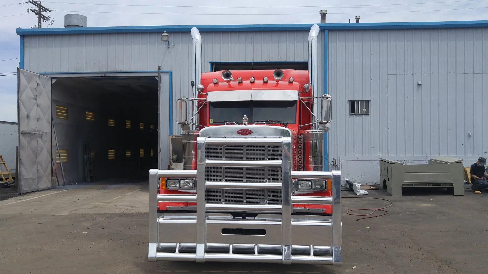 Red semi truck parked in front of an industrial warehouse loading bay