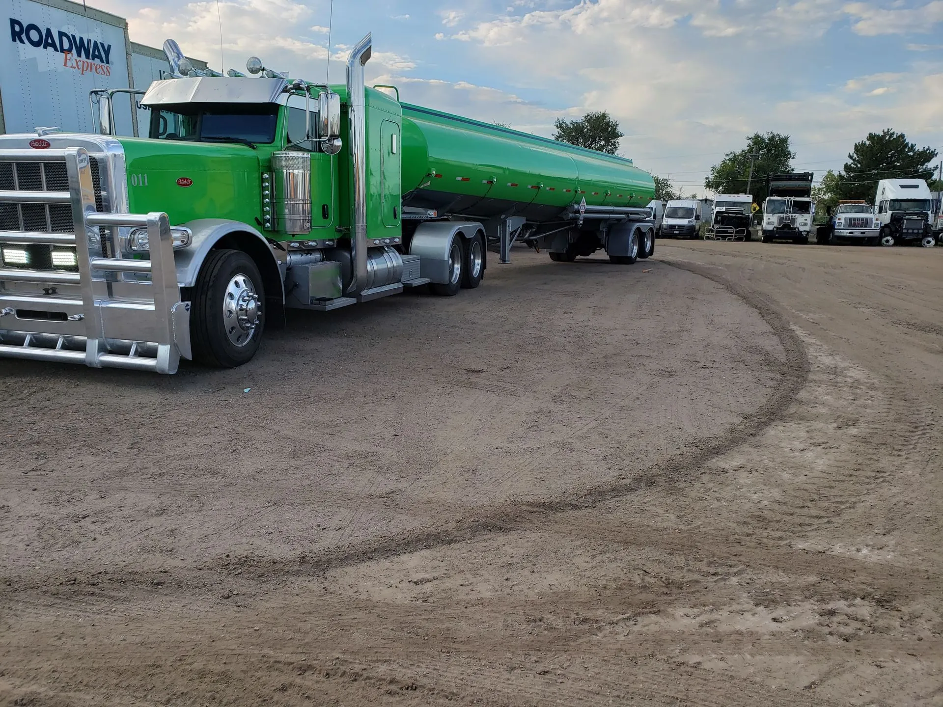 Green tanker truck parked on a dirt lot with several white trucks in the background