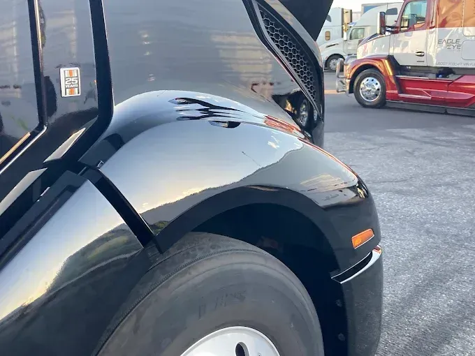 Close-up of a black truck’s front wheel and fender in a parking lot, with another truck in the background.