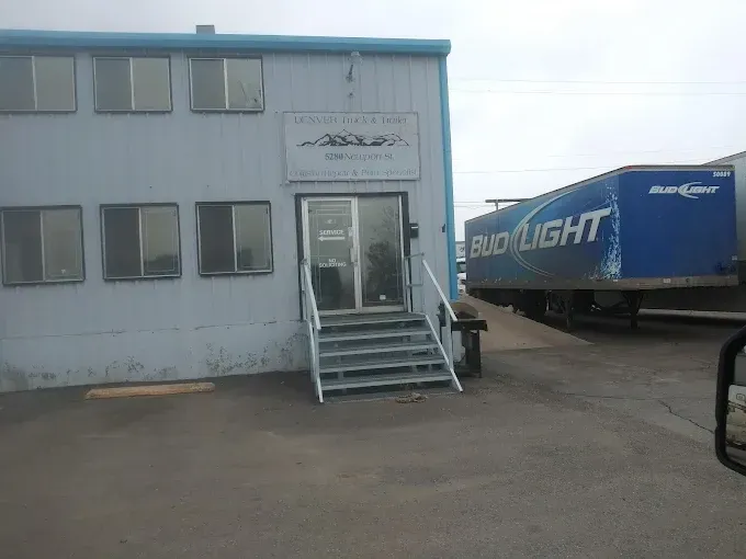 Small white building with stairs and entrance, next to a blue Bud Light trailer in a parking lot.