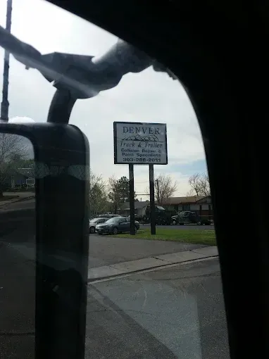 Street sign reading "Dewsbury" near parked cars, seen through a vehicle window.
